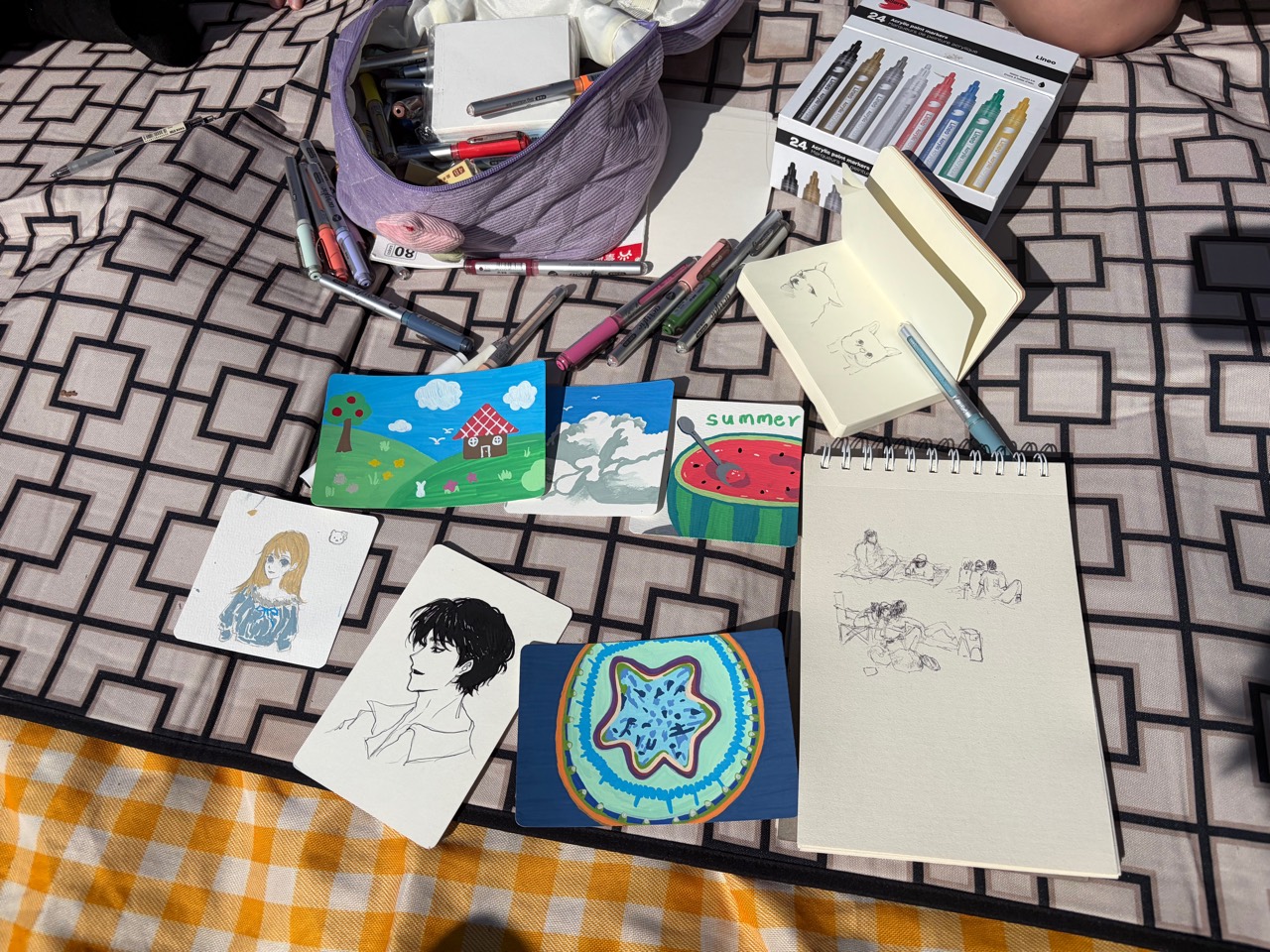 Drawings, sketchbooks, and art supplies spread across an outdoor table